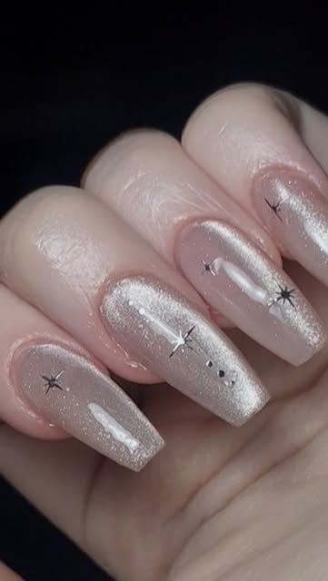 Coleccion Estrella. Unas largas nude nacaradas con reflejo de cat eye plateado, y estrellitas negras de cuatro puntas repartidas por encima.