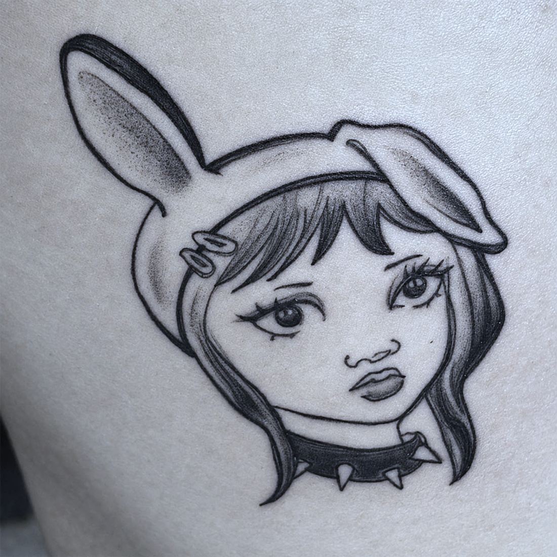 Tatuaje en la pierna. Una chica de estilo comic con orejas de conejo y una gargantilla de pinchos, resuelta a linea fina con sombreado suave.