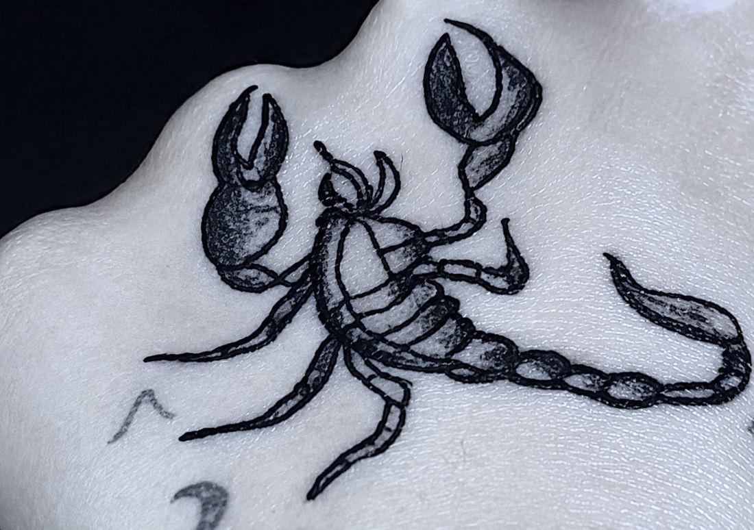 Tatuaje en el lateral de la mano. Un escorpion con las pinzas abiertas y la cola levantada, hecho a linea y negro.